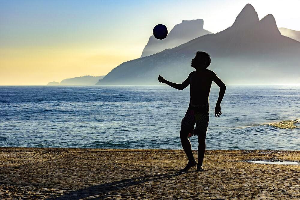 Boy playing soccer in front of the sea and hills during sunset, Ipanema, Rio de Janeiro, Rio de Janeiro, Brasil