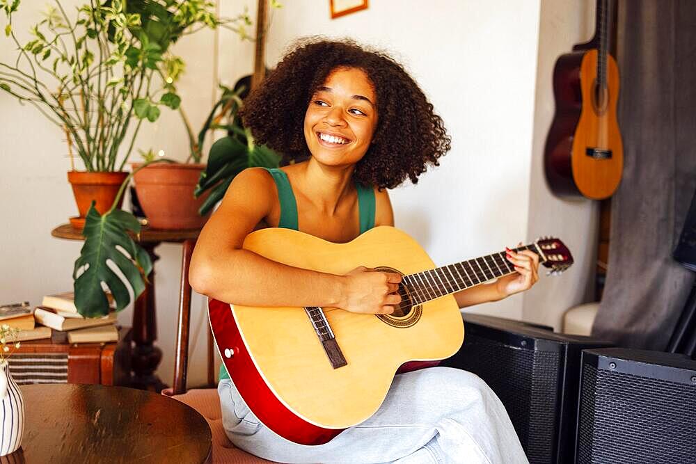 Smiling afro americal young woman playing acoustic guitar. Girl playing the guitar