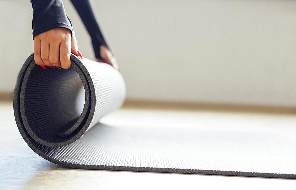 Side view of crop anonymous slim female unrolling mat for yoga practice in white studio