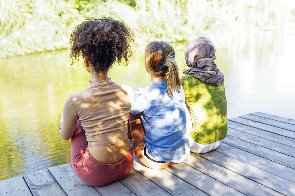 Rear view of multiracial young teen female friends resting in the park after sport training and having fun together. Diversity, sport and friendship concept