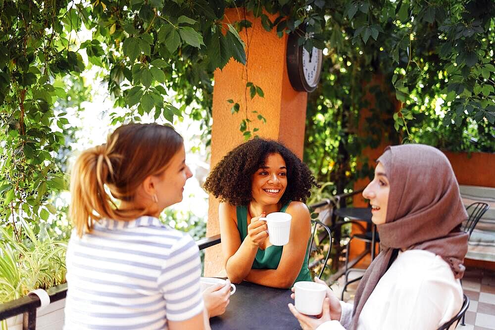 Multiethnic group of girls wearing casual clothes and traditional hijab bonding and having fun outdoors. Three young teen girls in garden cafe drinking tea or coffee