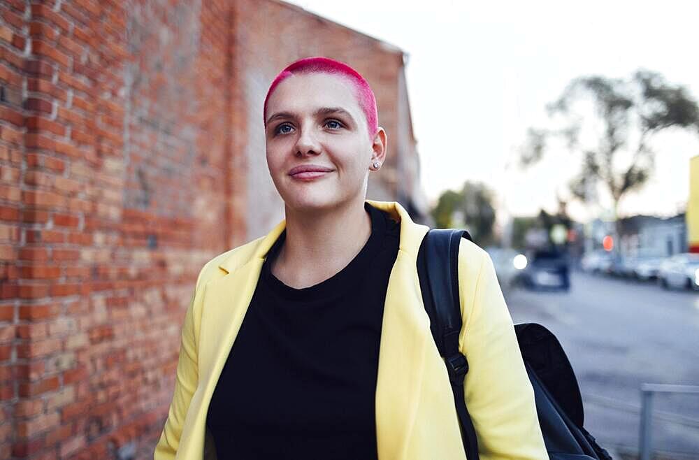 Young redhaired bald woman on the street. Girl with short shaved hair walking in the evening in the city center