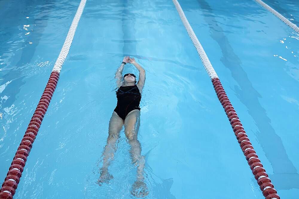 Portrait of a fit woman catcher in the pool. Portrait of a competitive female catcher near the use. Young swimmer wears a swim cap and puts away goggles