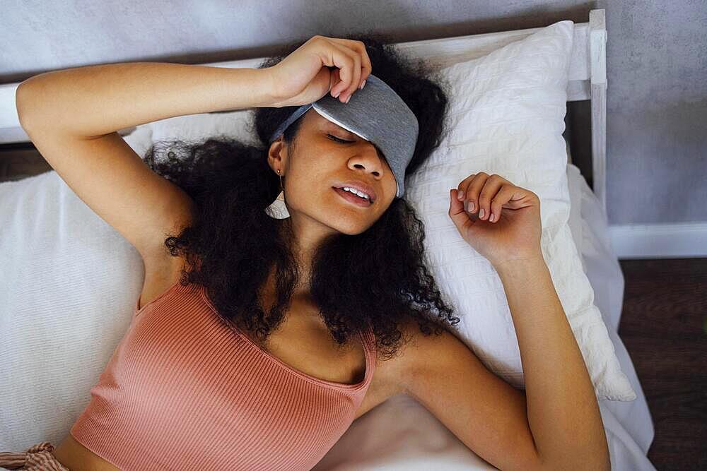 African American young woman wear pajamas sleeping on the bed at home, closed eyes, taking a break. Black millennial girl resting, top view. Relax, doze, lazy day