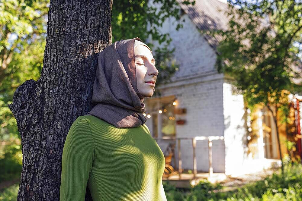 Muslim teen girl hugging a tree. Close up portrait of a young female in a hijab and casual clothes in the park. Protecting the environment and caring for plants concept