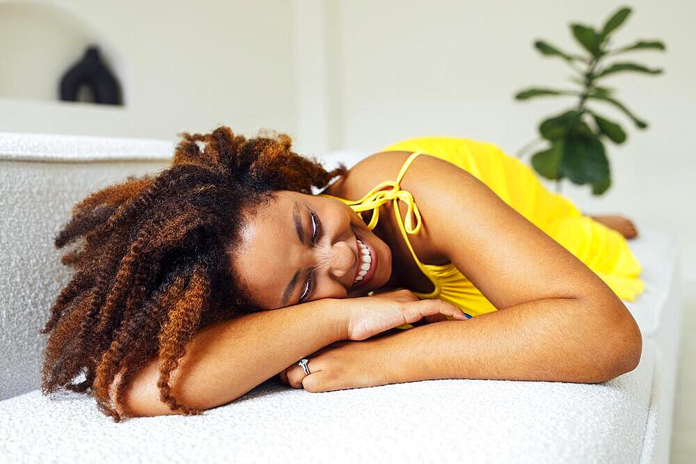 Beautiful curvy oversize young afto american woman in a yellow dress lies on a sofa at home. Body positive stylish smiling female have relax time. Body acceptance and diversity concept. Copy space