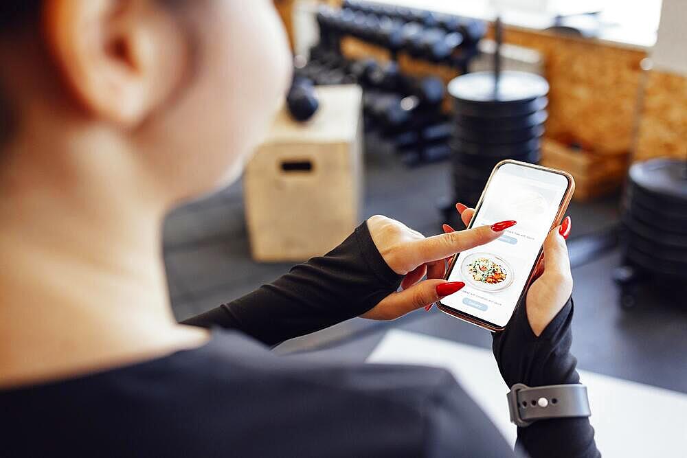 Fitness App. Sporty Fit Young Lady Holding And Pointing At Smartphone With fitness app While Training indoors. Smiling Woman Demonstrating screen of mobile phone