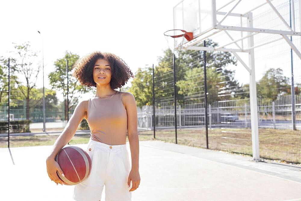 Mixed-race young smiling female outdoors and having fun. Stylish cool teen girl gathering at basketball court, playing basketball outdoors