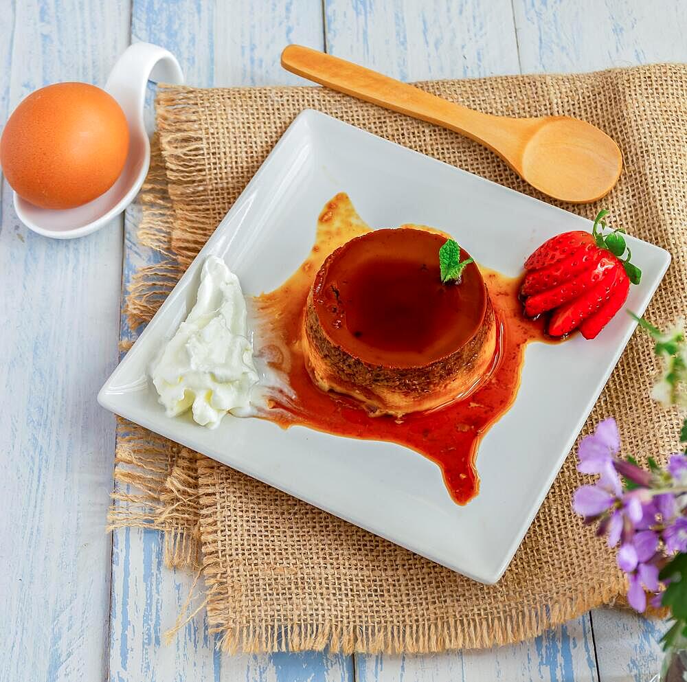 Egg custard with cream and strawberries on a white plate on a blue wooden table with flowers