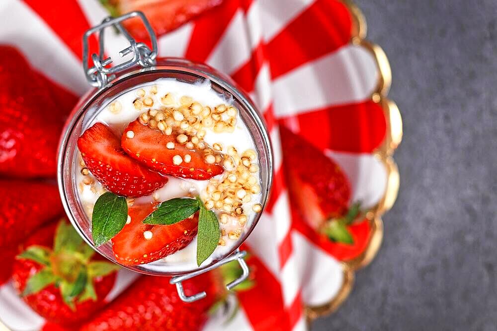 Top view of healthy strawberry fruit dessert with yogurt and puffed quinoa grains on red and white striped plate