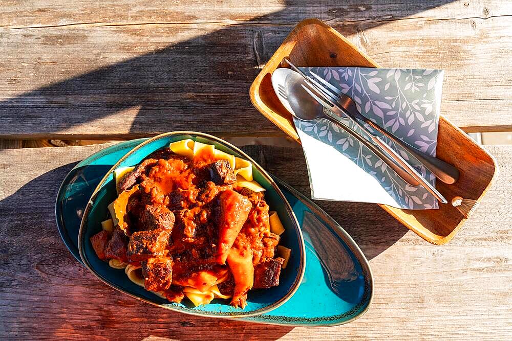 Plate of goulash with noodles and cutlery on a wooden table, Landgasthof zum Gruenen Baum, Ringenwalde village, Uckermark, Brandenburg, Germany, Europe