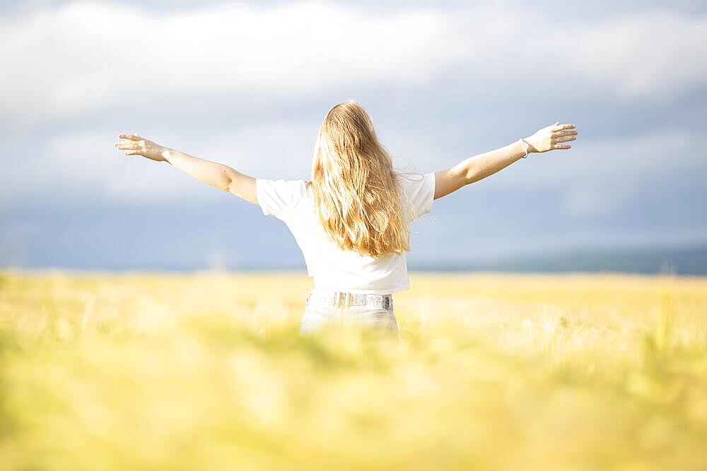 A young girl walks through a cornfield on a sunny warm day and spreads out her arms