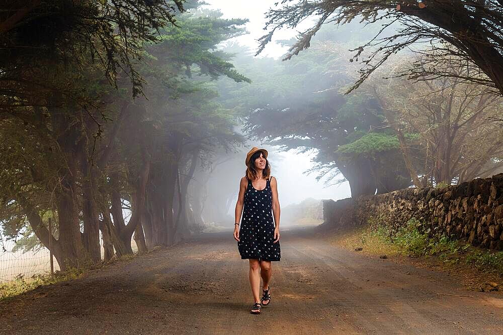 A woman enjoying walking through foggy trees towards the juniper forest in El Hierro. Canary Islands