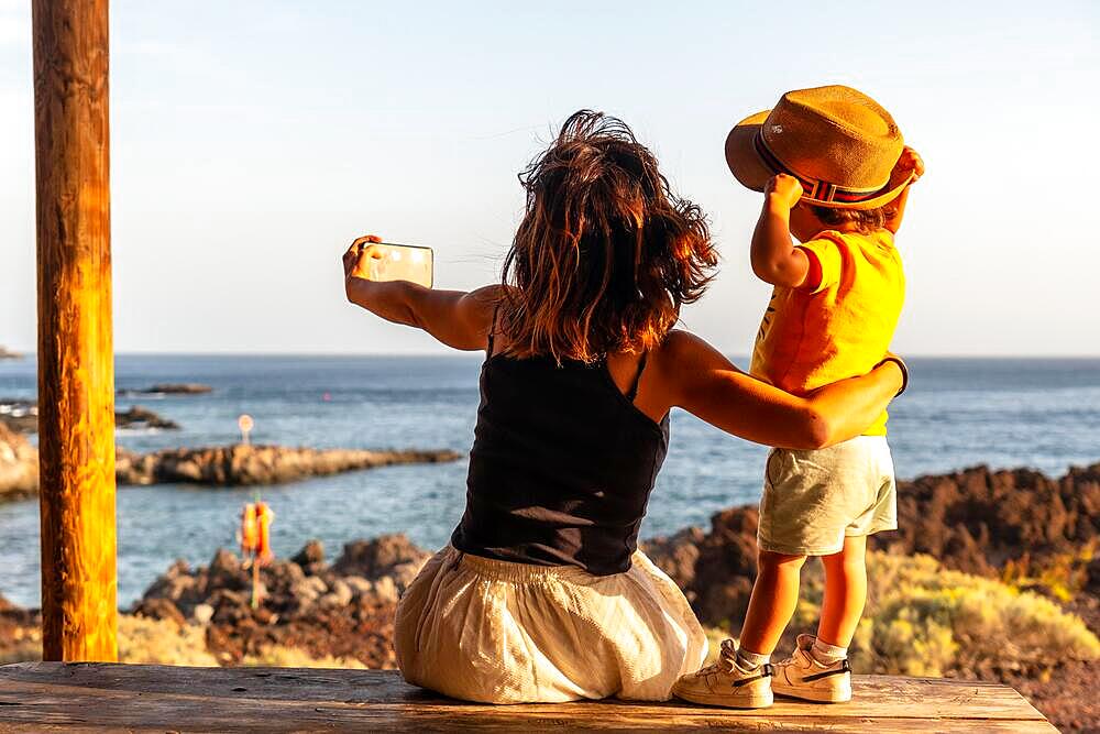 Mother and son on vacation taking a photo on Tacoron beach in El Hierro, Canary Islands. Having fun, boy in a hat