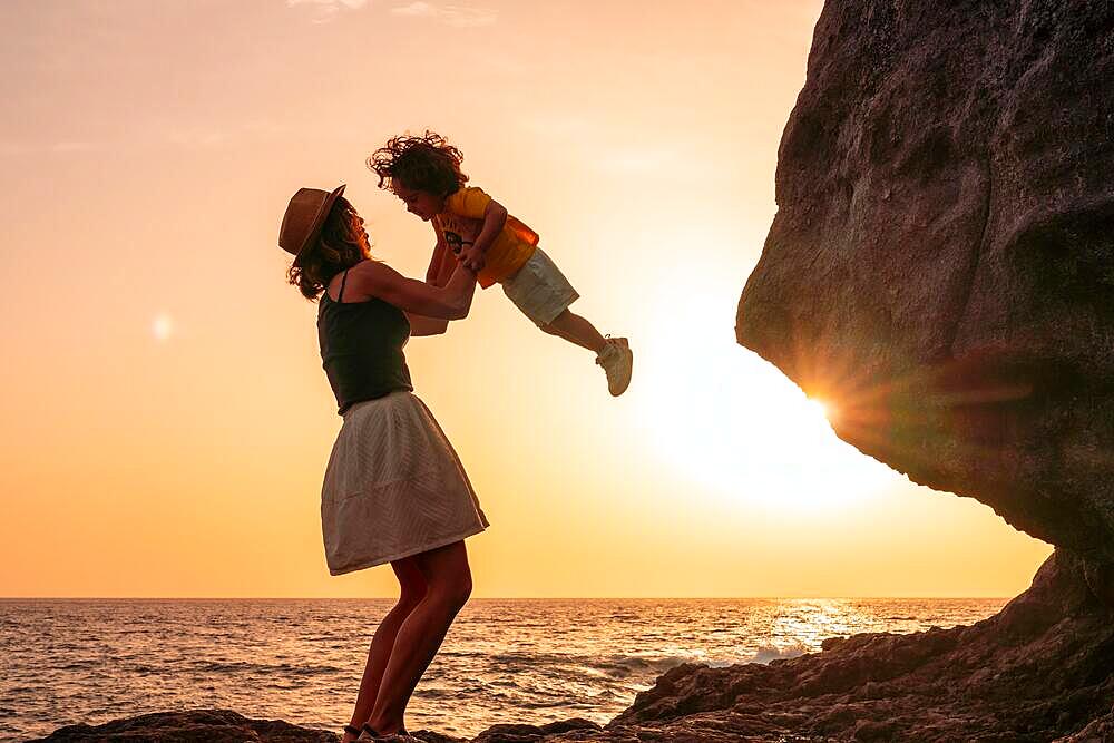 Silhouette of mother and son having fun lifting the son into the sunset on the beach of Tacoron on El Hierro, Canary Islands, vacation concept, orange sunset