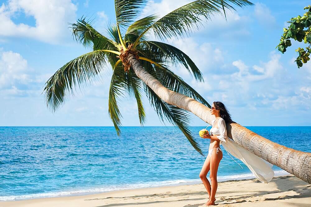 Pretty young woman enjoy her tropical beach vacation standing under palm tree. Summer concept