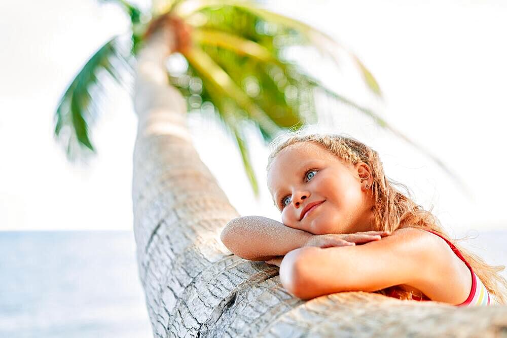 Happy dreaming beautiful child relax on tropical beach with palm tree. Carefree concept