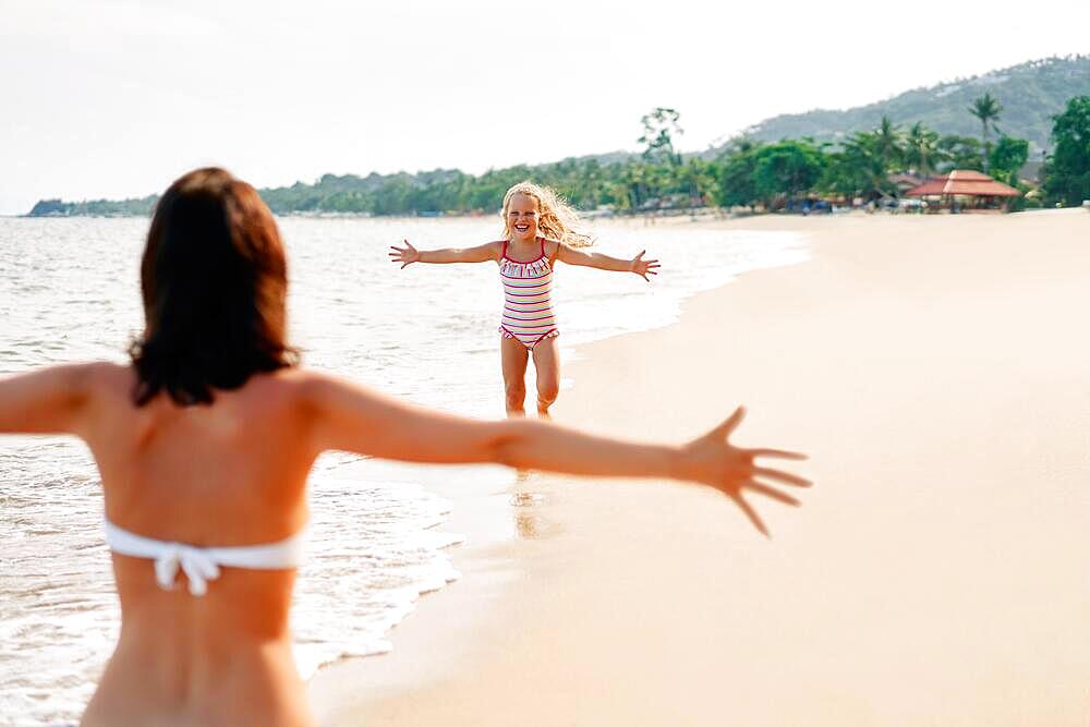 Happy little girl run to her mother for hugs on tropical beach. Summer vacation, happy family, love concept