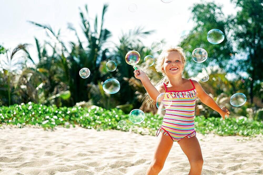 Little happy girl playing soap bubbles on the topical beach. Childhood, lifestyle concept