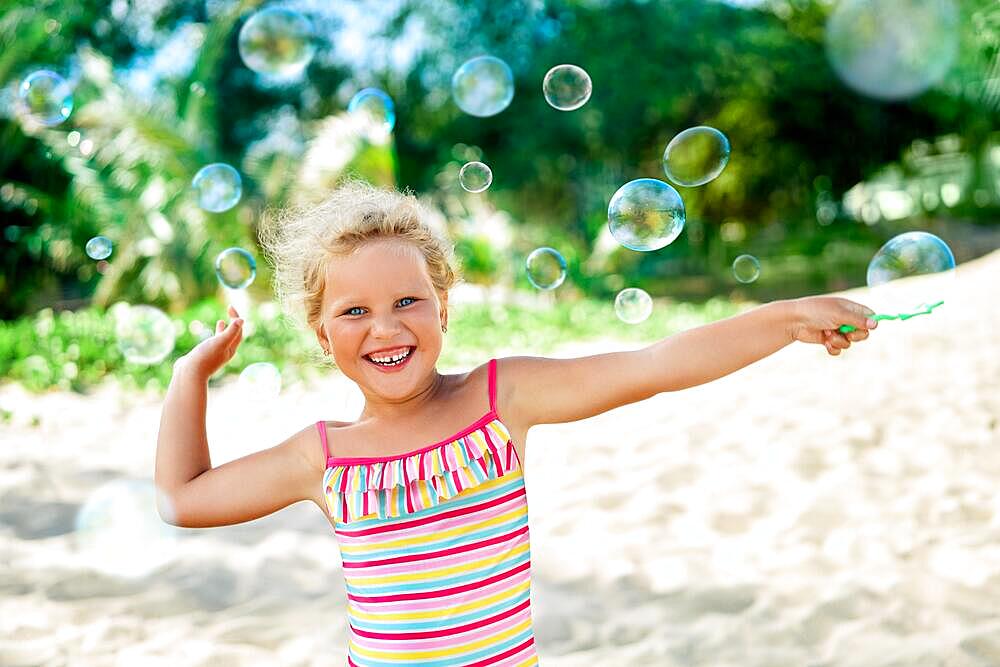 Little happy girl playing soap bubbles on the topical beach. Childhood, lifestyle concept