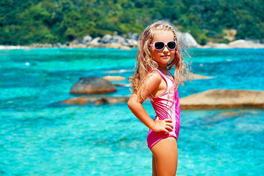 Cute little girl in sun glasses posing on beautiful tropical beach. Summer, fun and vacations concept