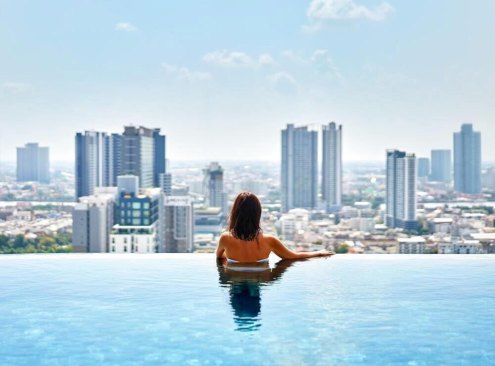 Young woman relax on the edge of the roof top swimming pool. Summer vacation concept