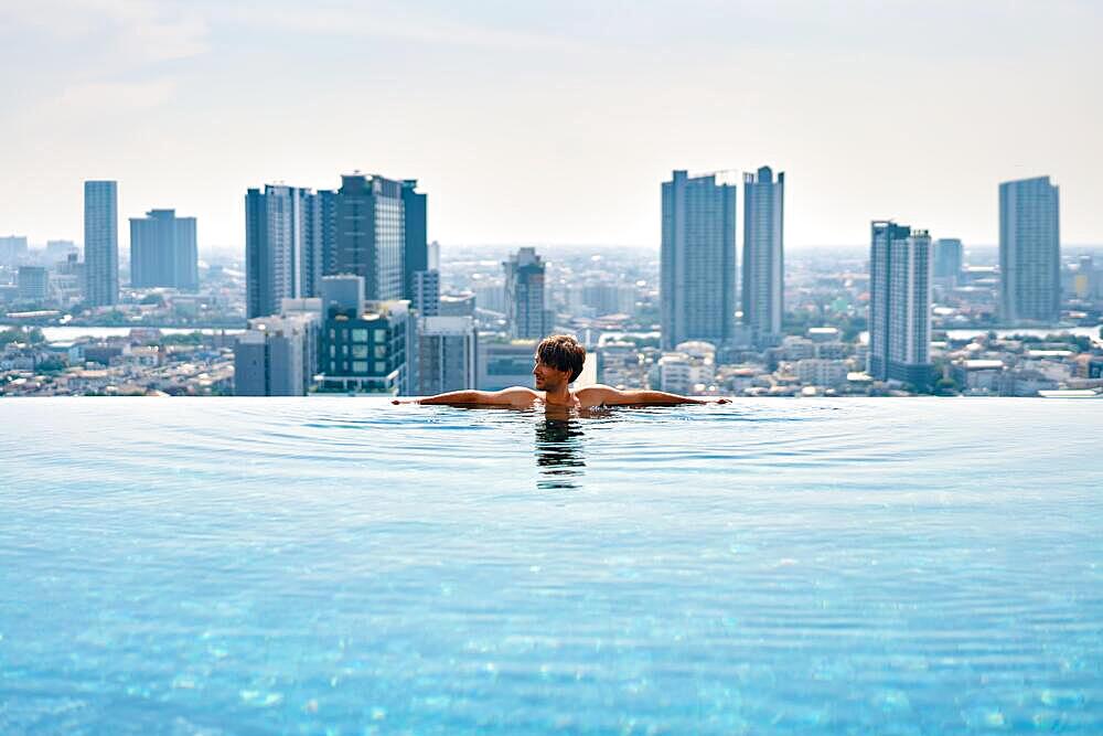 Young man relax on the edge of swimming pool in roof top of hotel. Summer vacation concept