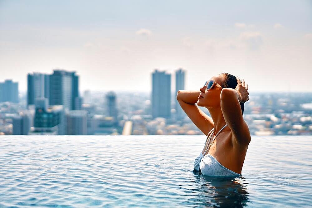 Young beautiful woman enjoy summer vacation on swimming pool in hotel roof top . Travel and relax concept