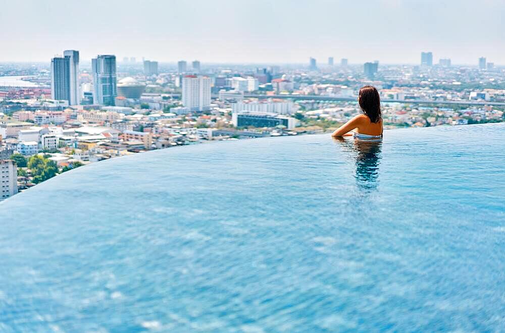 Young woman relax on the edge of the roof top swimming pool. Summer vacation concept