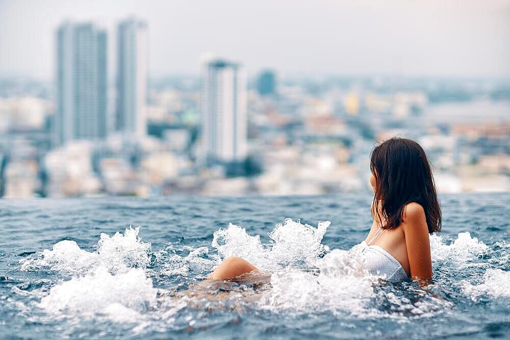 Young woman relaxing in jacuzzi on the rooftop of hotel and enjoying city view. Summer vacation concept