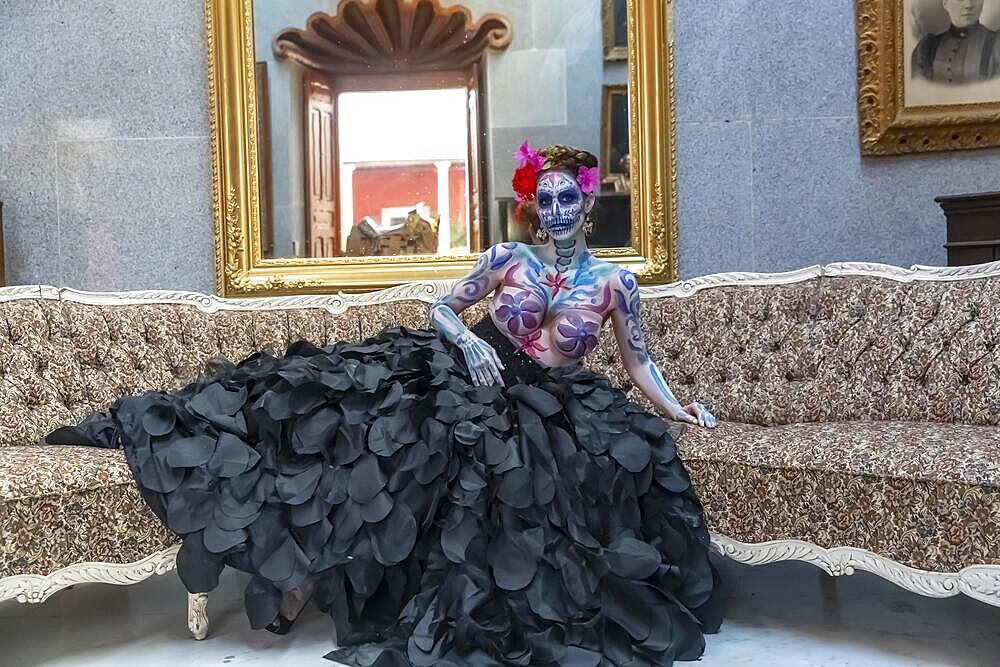 A gorgeous Hispanic Brunette model poses with traditional skull sugar makeup paint for a Mexican festival