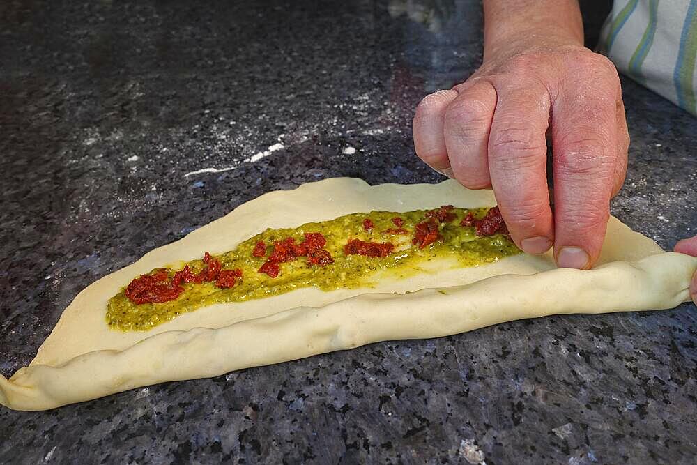 Swabian cuisine, preparing hearty party yeast plait, salty yeast plait, yeast pastry, yeast yeast dough with herb paste and dried tomatoes, pesto, rolling up raw dough, vegetarian, man's hand, countertop, typical Swabian reinterpreted, traditional cuisine, food photography, studio, Germany, Europe