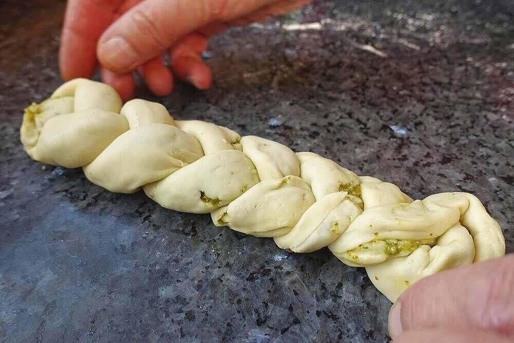 Swabian cuisine, preparing hearty party yeast plait, savoury yeast plait, yeast pastry, yeast yeast dough filled with herb paste and dried tomatoes, pesto, braiding raw dough, making plait from three strands, vegetarian, men's hands, worktop, typical Swabian reinterpreted, traditional cuisine, food photography, studio, Germany, Europe