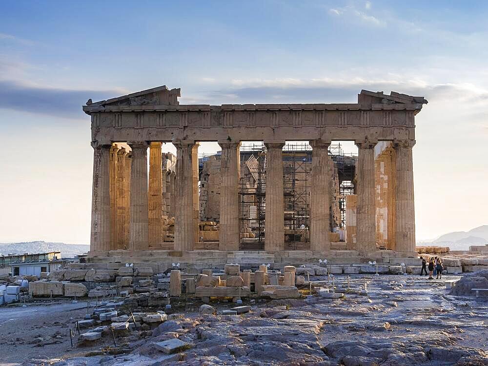 Frontal view of Parthenon on Acropolis, Athens, Greece against sunset, clear blue sky and few tourists taking photos of ruins