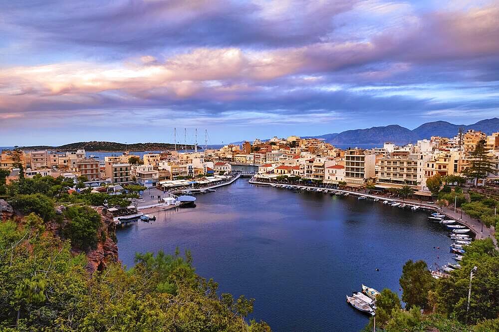 Colorful view of Voulismeni lake and Agios Nikolaos town on Crete island, Greece at summer sunset. Boats, cafes, restaurants, ship, marina, promenade