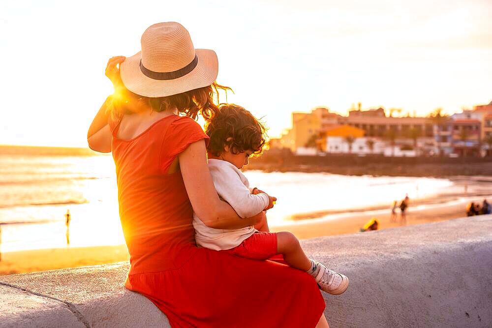 Mother and son at sunset on the beach of Valle Gran Rey village in La Gomera, Canary Islands. sitting looking at the sea