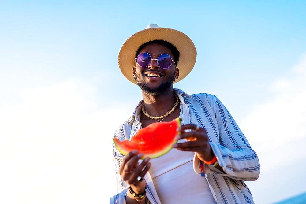 Black ethnic man enjoy summer vacation at the beach eating a watermelon