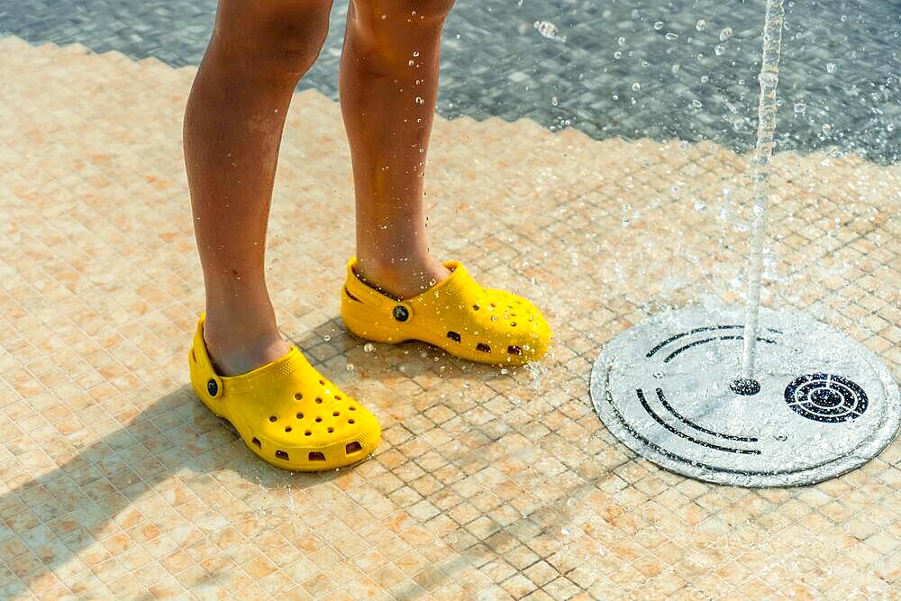 Children enjoying summer pool with water jets, summer vacation. Yellow child's flip flops