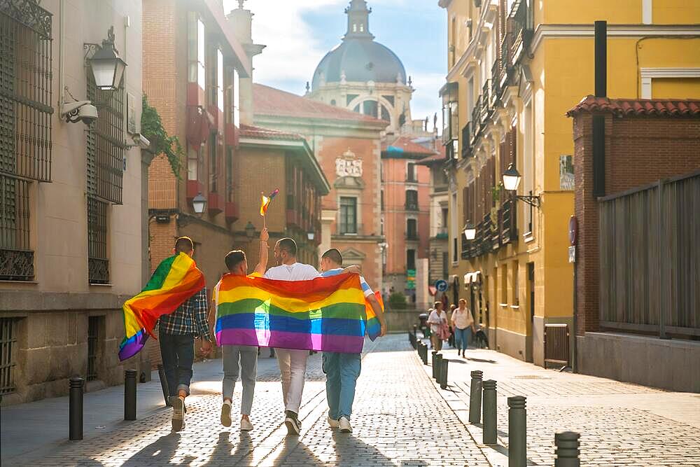 Man with his back facing the demonstration with rainbow flags at sunset, gay pride party in the city, lgbt concept