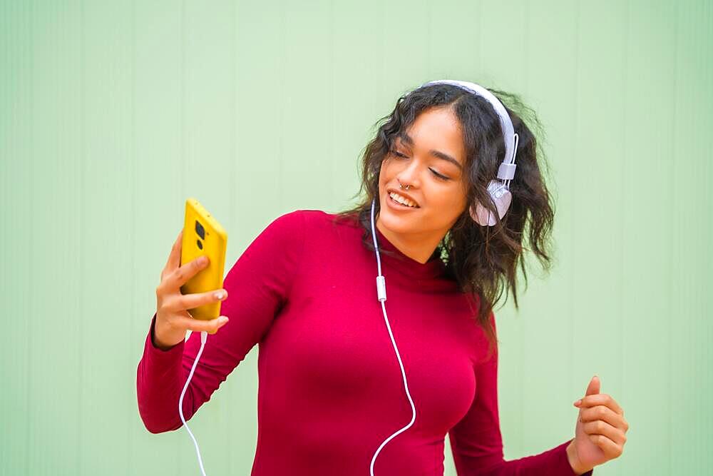 Portrait of latin woman with headphones smiling, technology concept on a green background, listening to music