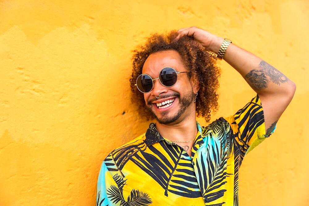 Man with afro hair in summer summer in a palm tree shirt on a yellow background