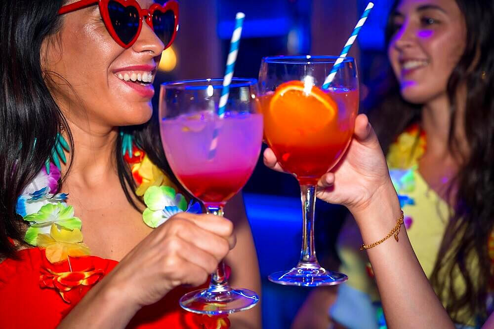 Female friends in a nightclub toasting with glasses of alcohol smiling at a night party