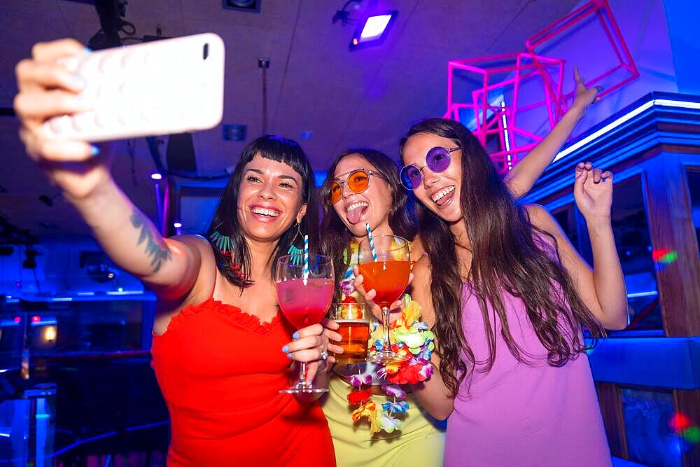 Friends with glasses of alcohol in a nightclub taking a selfie at a night party in a pub