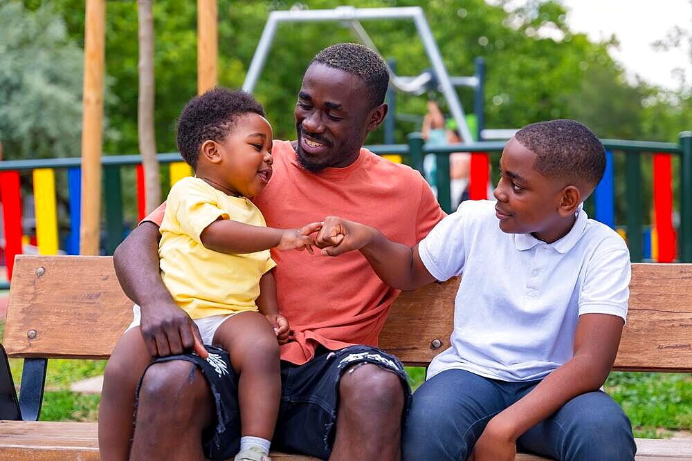 African black ethnicity father having fun with his children in playground of city park