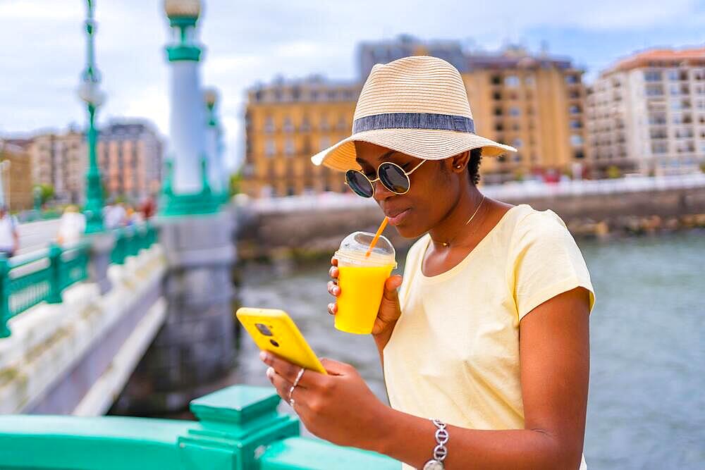 Black ethnic woman having an orange juice in the city, tourist enjoying the summer