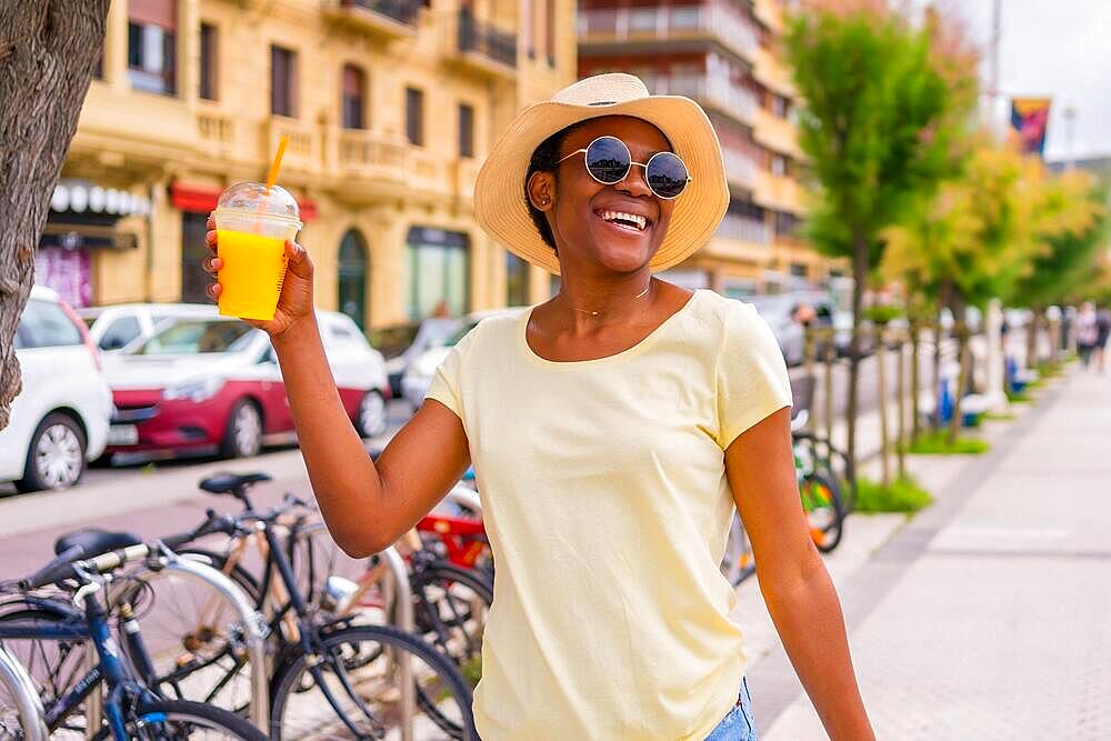 Black ethnic woman having an orange juice enjoying the summer in the city