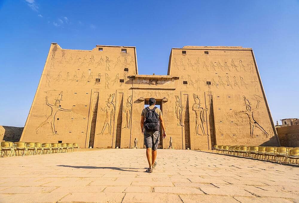 A young tourist entering the Temple of Edfu in the city of Edfu, Egypt. On the bank of the Nile river, geco-Roman construction, temple dedicated to Huros