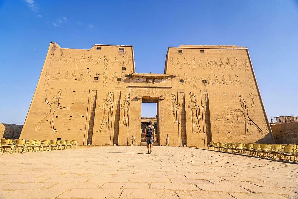 A young tourist entering the Temple of Edfu in the city of Edfu, Egypt. On the bank of the Nile river, geco-Roman construction, temple dedicated to Huros