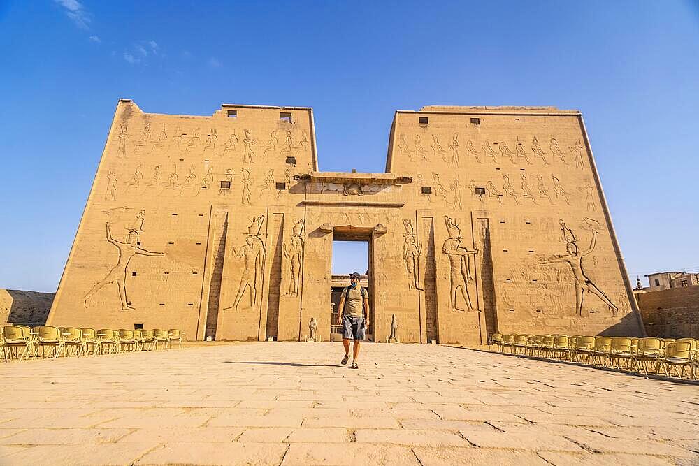 A young tourist entering the Temple of Edfu in the city of Edfu, Egypt. On the bank of the Nile river, geco-Roman construction, temple dedicated to Huros