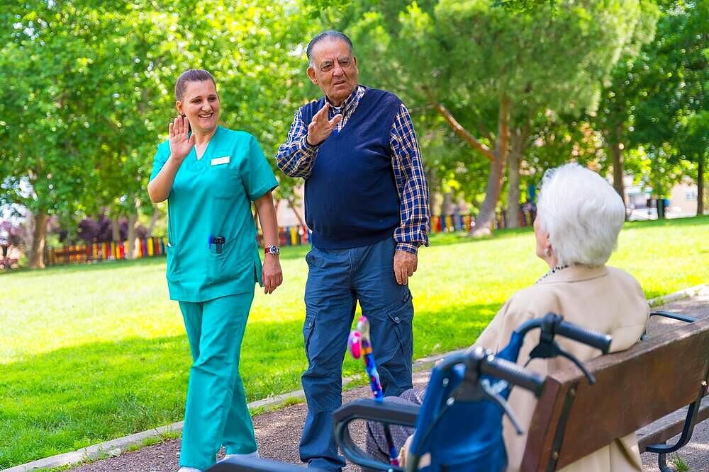 An elderly man with the nurse on a walk through the garden of a nursing home greeting an elderly woman